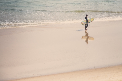 Surfer walking the water line at a beach - Australian Stock Image