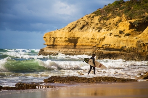 Surfer walking through shallows to a surf break - Australian Stock Image