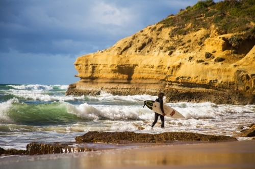 Surfer walking through shallows to a surf break