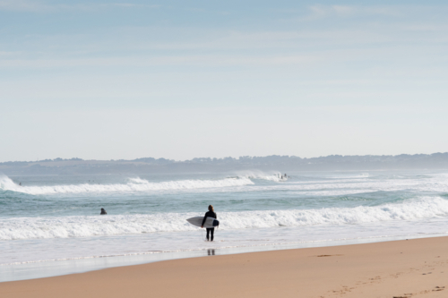 Surfer with board on edge of water looking out to sea - Australian Stock Image