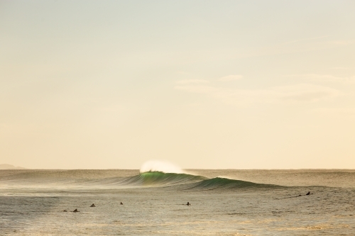 Surfers in the distance with breaking wave - Australian Stock Image