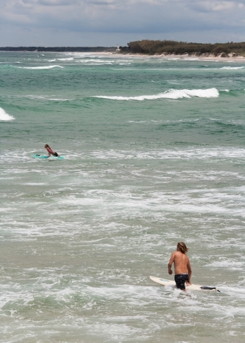 Surfers wading and padding out to a surf break
