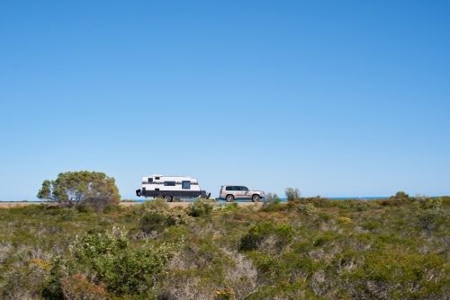 SUV towing a caravan along a coastal road in Western Australia under blue skies, with motion blur.