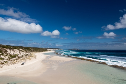 Sweeping coastal view with 4wd vehicle on beach, dark blue ocean and polarised sky