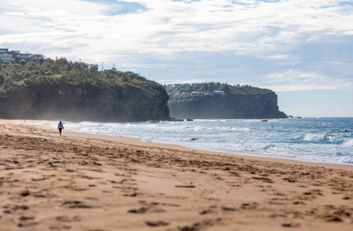 Sydney Beach scene with woman walking in distance towards the cliffs - Australian Stock Image