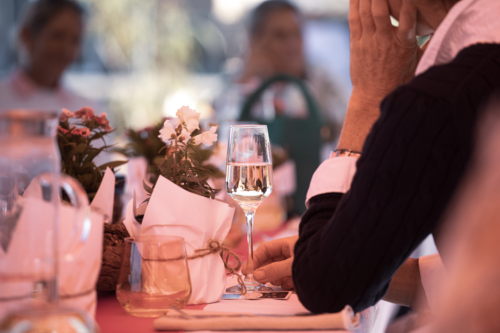 Table setting with wine glass and flowers, and people in the background - Australian Stock Image