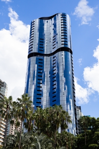 tall curved skyscraper with mirrored surface reflecting white clouds and blue sky