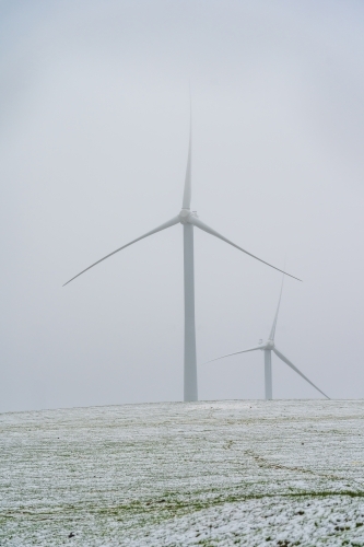 Tall wind turbines in a foggy sky on a snow covered hilltop - Australian Stock Image
