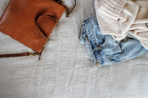 Tan leather bag with jeans and cream woollen jumper on grey linen - Australian Stock Image