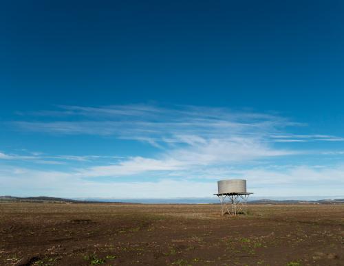 Tank stand in a treeless paddock against blue sky - Australian Stock Image
