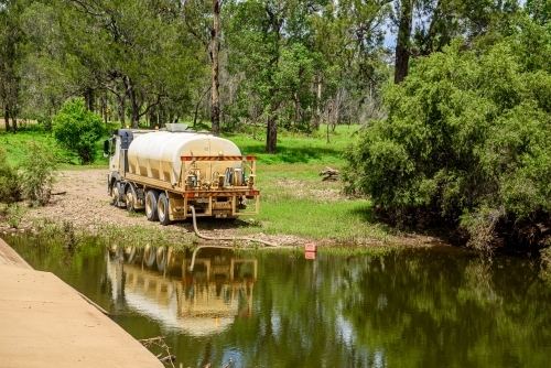Tanker truck pumping fresh water from a creek next to a concrete flood way - Australian Stock Image