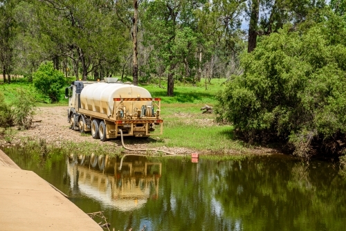 Tanker truck pumping fresh water from a creek next to a concrete flood way