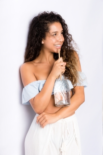 Tanned, happy young woman, white background, drinking water from a glass bottle
