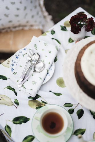 Tea, cake, and cutlery resting on patterned cloth in the soft outdoor light. - Australian Stock Image