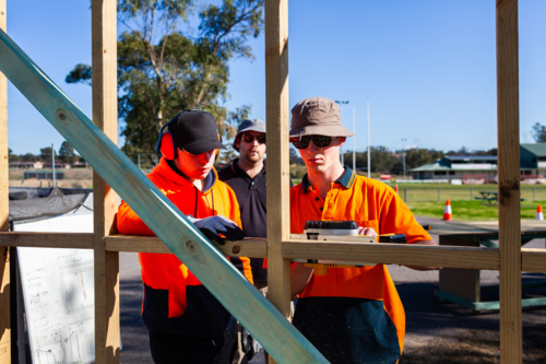teacher instructing trade apprentices on using planer tool on building frame - Australian Stock Image
