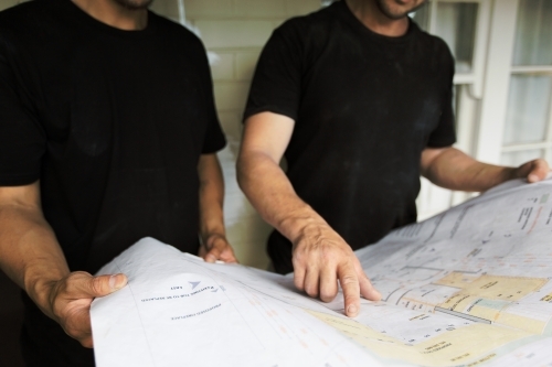 Team members pointing at architectural drawing and problem solving at construction site - Australian Stock Image
