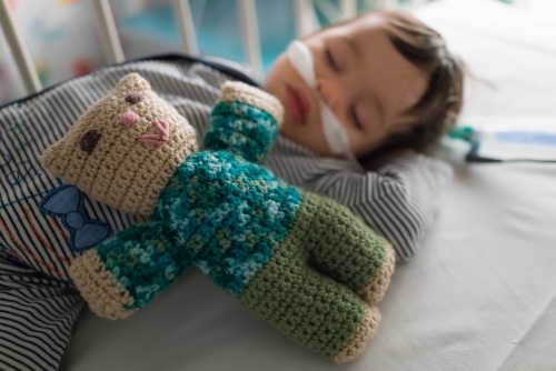 Teddy lying on a sleeping one year old being treated with oxygen therapy - Australian Stock Image