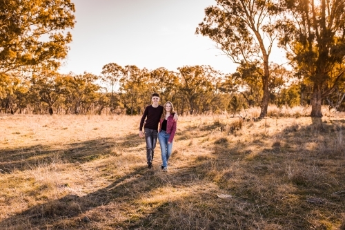 Teen boy and girl walking through paddock arm in arm smiling happy - Australian Stock Image