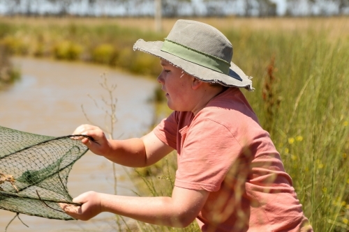 Teen boy casting yabby net into channel on rural property - Australian Stock Image