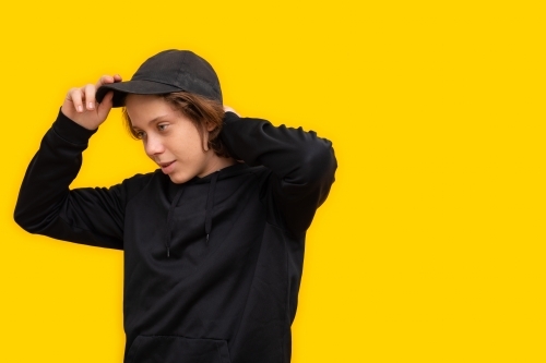 teen boy dressed in black with cap on yellow background - Australian Stock Image