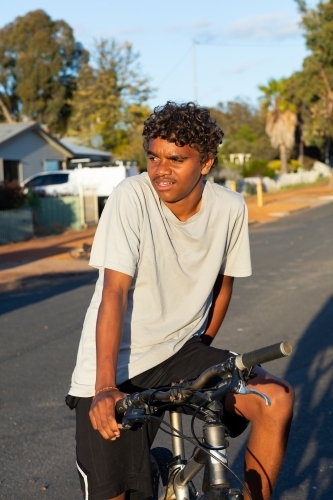 teen boy resting on bike in street - Australian Stock Image