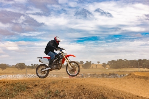 Teen boy riding motorbike over hill at motocross track meet - Australian Stock Image
