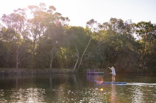 Teen boy riding stand up paddle board in golden afternoon light