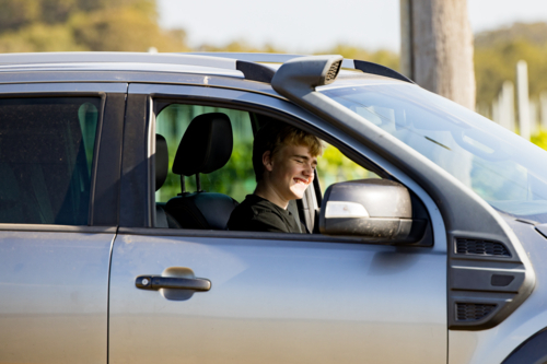 Teen boy sitting in car smiling at vineyard - Australian Stock Image