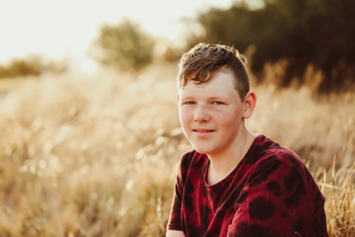 Teen boy sitting in long dry grass in golden afternoon light - Australian Stock Image