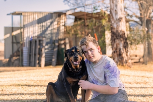 Teen boy sitting on grass with pet Rottweiler dog - Australian Stock Image