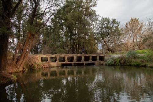 Teen boy walking across low bridge over the Cudgegong River in rural New South Wales - Australian Stock Image