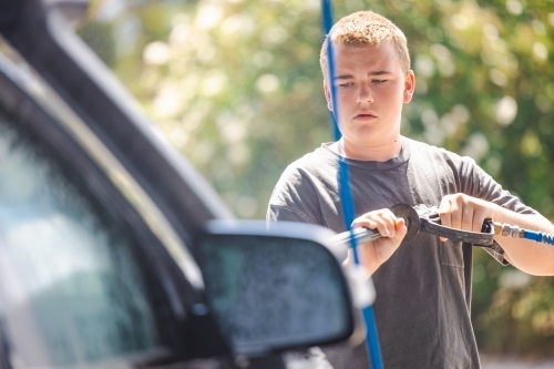 Teen boy washing vehicle in self-service car wash bay