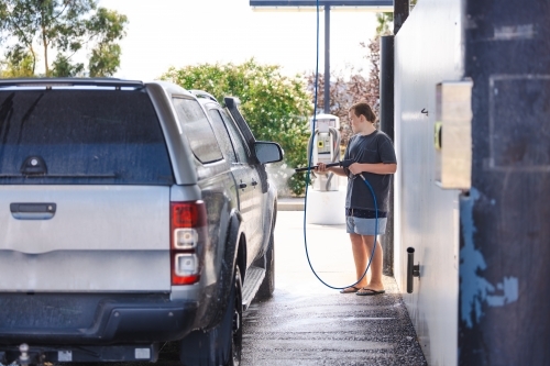 Teen boy washing vehicle in self-service car wash bay - Australian Stock Image