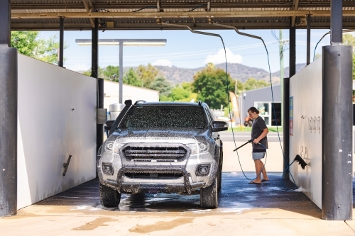 Teen boy washing vehicle in self-service car wash bay - Australian Stock Image