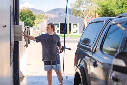 Teen boy washing vehicle in self-service car wash bay - Australian Stock Image
