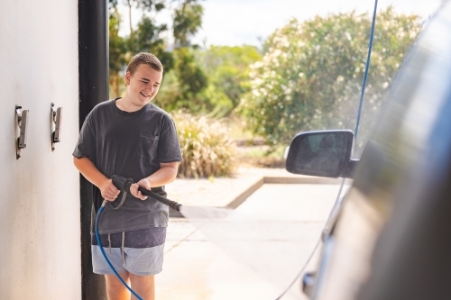 Teen boy washing vehicle in self-service car wash bay - Australian Stock Image