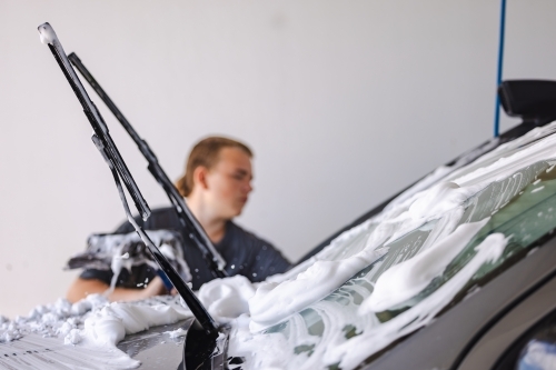 Teen boy washing vehicle in self-service car wash bay - Australian Stock Image