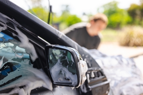 Teen boy washing vehicle in self-service car wash bay - Australian Stock Image