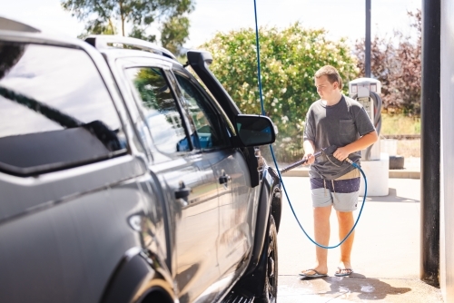 Teen boy washing vehicle in self-service car wash bay - Australian Stock Image