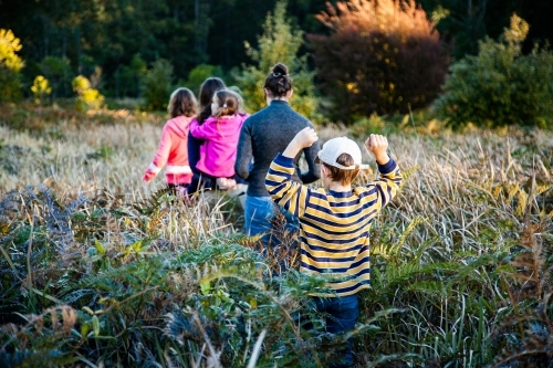Teen cousins and younger siblings adventure through fern undergrowth in forest - Australian Stock Image