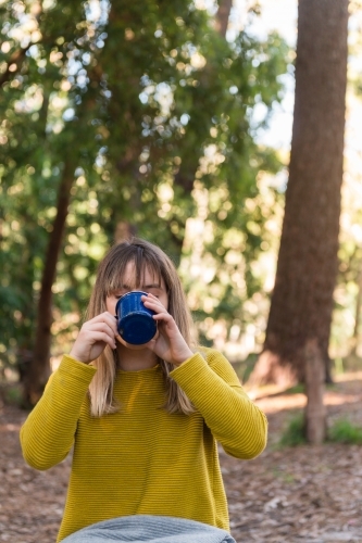 teen girl drinking from a mug on a picnic in the forest