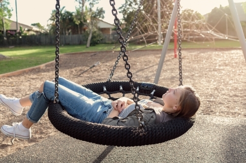Teen girl on big swing alone - Australian Stock Image