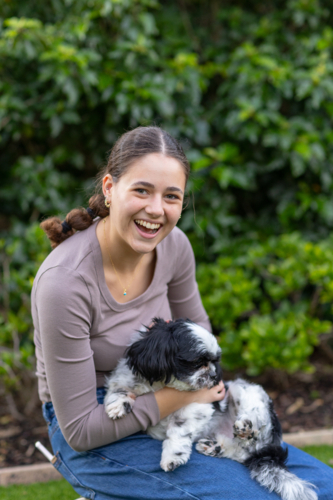 teen girl playing with pet dog in front of garden greenery - Australian Stock Image