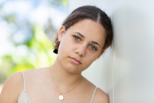 Teen girl resting her head on the white wall - Australian Stock Image