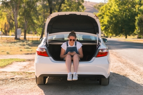 teen girl sitting in boot of car on a road trip - Australian Stock Image
