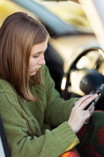 Teen girl sitting in car texting on smartphone - Australian Stock Image