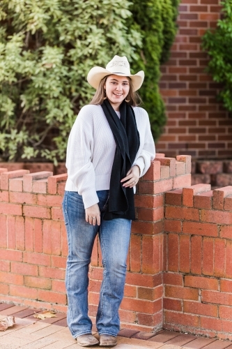 Teen girl standing leaning on brick wall smiling wearing hat and beanie - Australian Stock Image