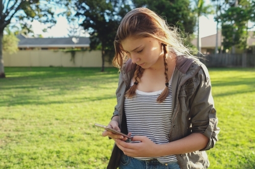 Teen girl using mobile phone while walking in the park - Australian Stock Image