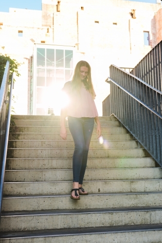 teen girl walking down stairs, backlit by a sun flare reflection - Australian Stock Image