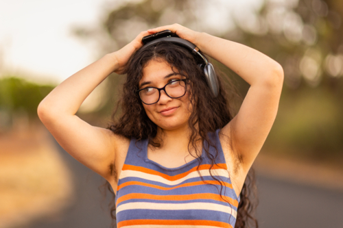 teen girl wearing headphones with hands on head revealing hairy armpits - Australian Stock Image